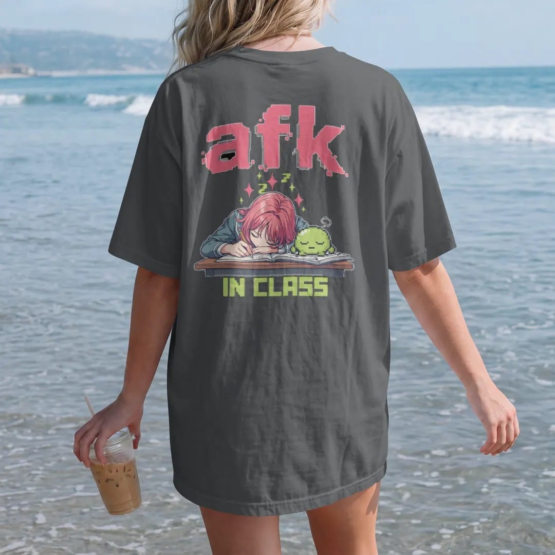 Woman on the beach in a Graphite tee, back view: an anime-style teen asleep on a desk with Blip the slime napping on a textbook and pixel Zs floating up, under afk in big pixel letters with in class below, in pink, lime, blue and silver.