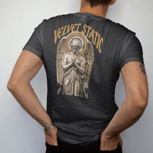 Man wearing a Black tee, seen from the back: a classical angel with folded wings and a halo of TV static in airbrushed chrome, under Velvet Static in tall gothic blackletter, in bone cream, chrome silver and antique gold.