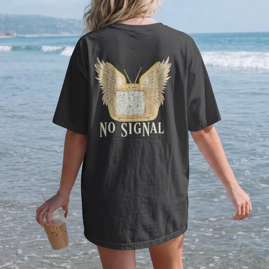 Woman on the beach in a Black tee, back view: a vintage cabinet television with angel wings and a screen full of static, above No Signal in widely spaced fashion serif capitals, in bone cream, chrome silver and antique gold.