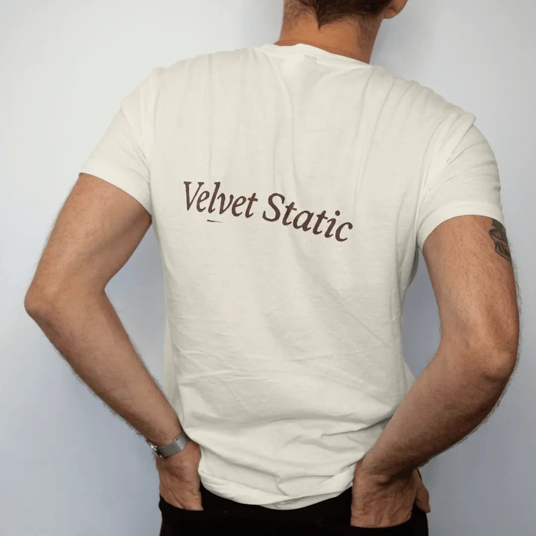Man wearing a Ivory tee, seen from the back: a single wordmark: Velvet Static in a large refined italic serif with a thin underline.
