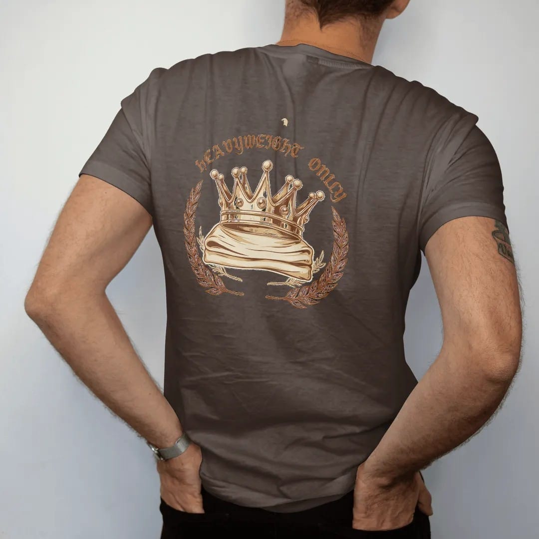 Man wearing a Espresso tee, seen from the back: a jeweled gold crown resting on a folded heavy tee between laurel branches, Heavyweight Only in blackletter above.
