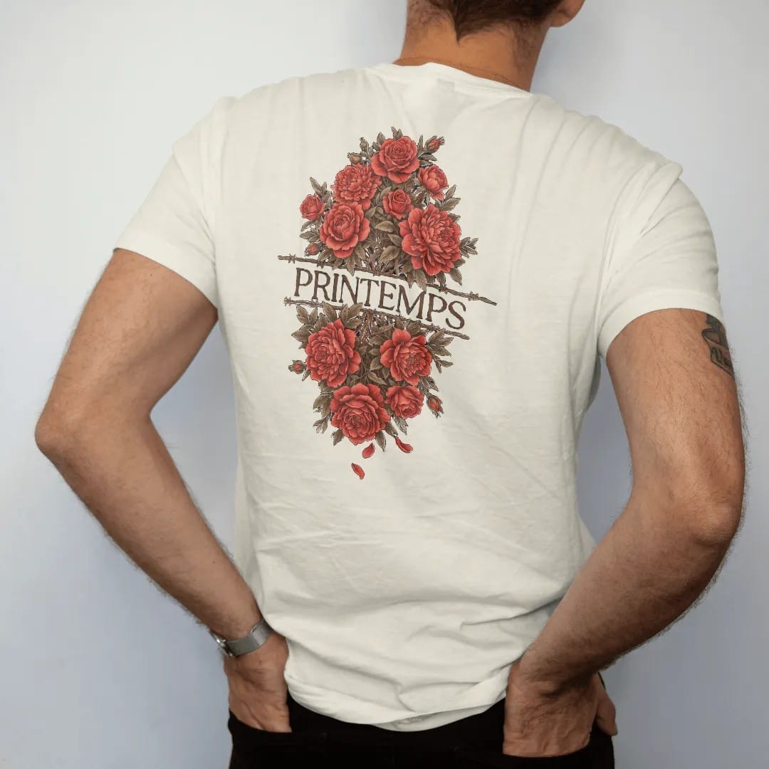 Man wearing a Ivory tee, seen from the back: roses and peonies blooming through a strand of barbed wire in engraved linework, with Printemps in fashion serif across the center, in espresso, oxblood and bronze.