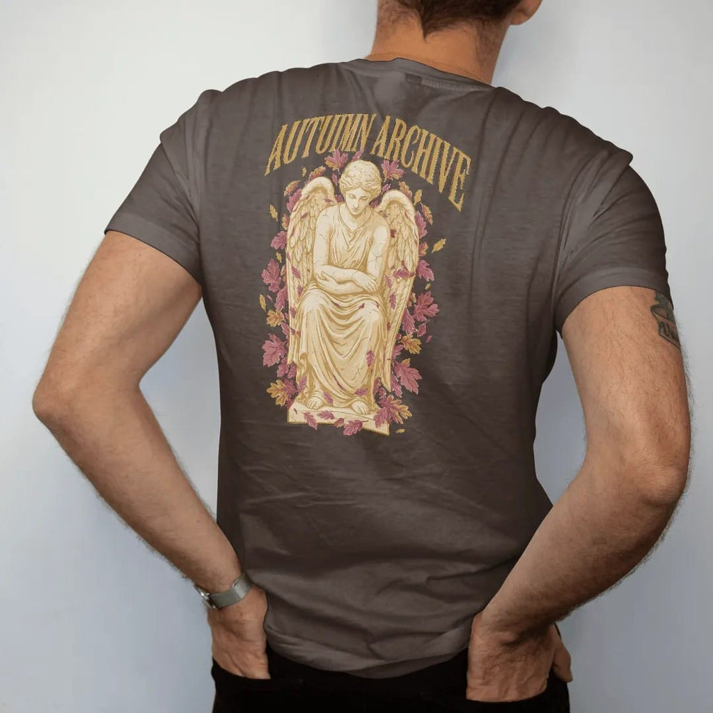 Man wearing a Espresso tee, seen from the back: a weathered marble angel seated with bowed head among falling oak and maple leaves, under Autumn Archive in gothic blackletter, in antique gold, dusty rose and bone cream.