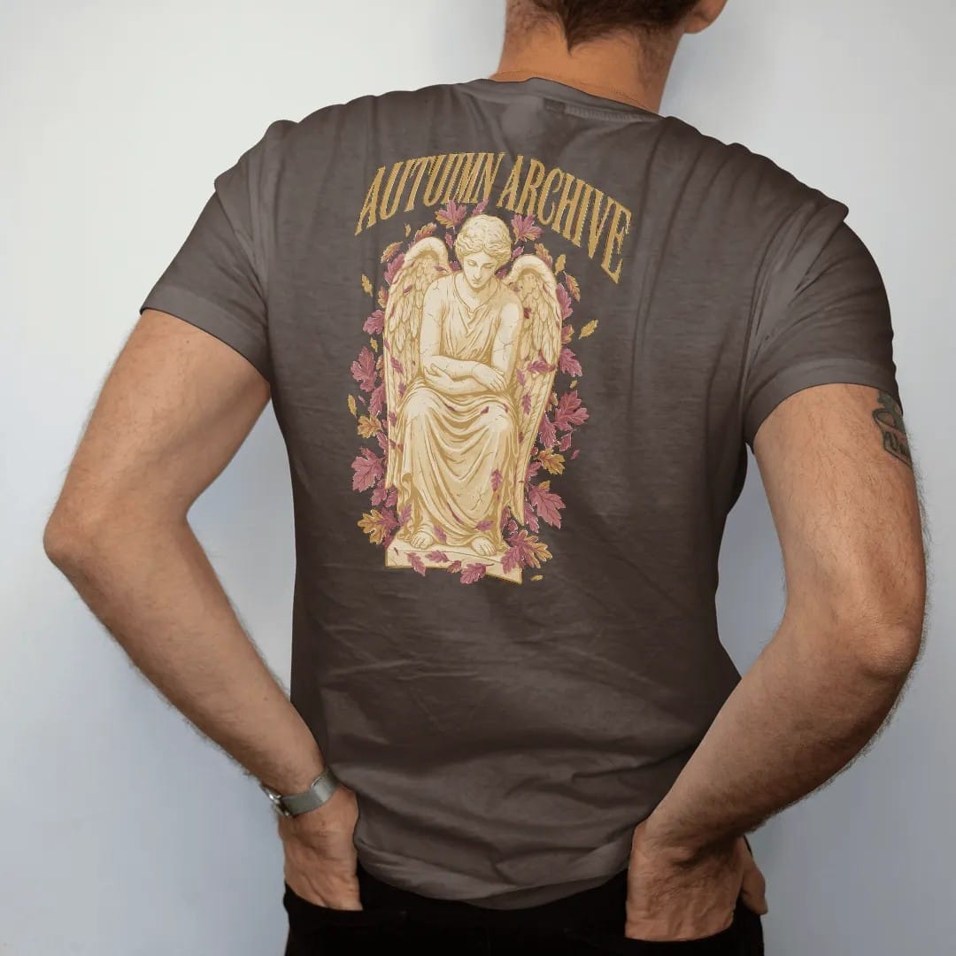 Man wearing a Espresso tee, seen from the back: a weathered marble angel seated with bowed head among falling oak and maple leaves, under Autumn Archive in gothic blackletter, in antique gold, dusty rose and bone cream.