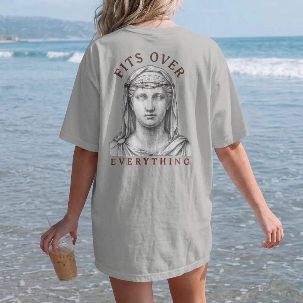 Woman on the beach in a Granite tee, back view: a classical marble angel bust with a barbed-wire crown, Fits Over arched above in serif and Everything spaced below.