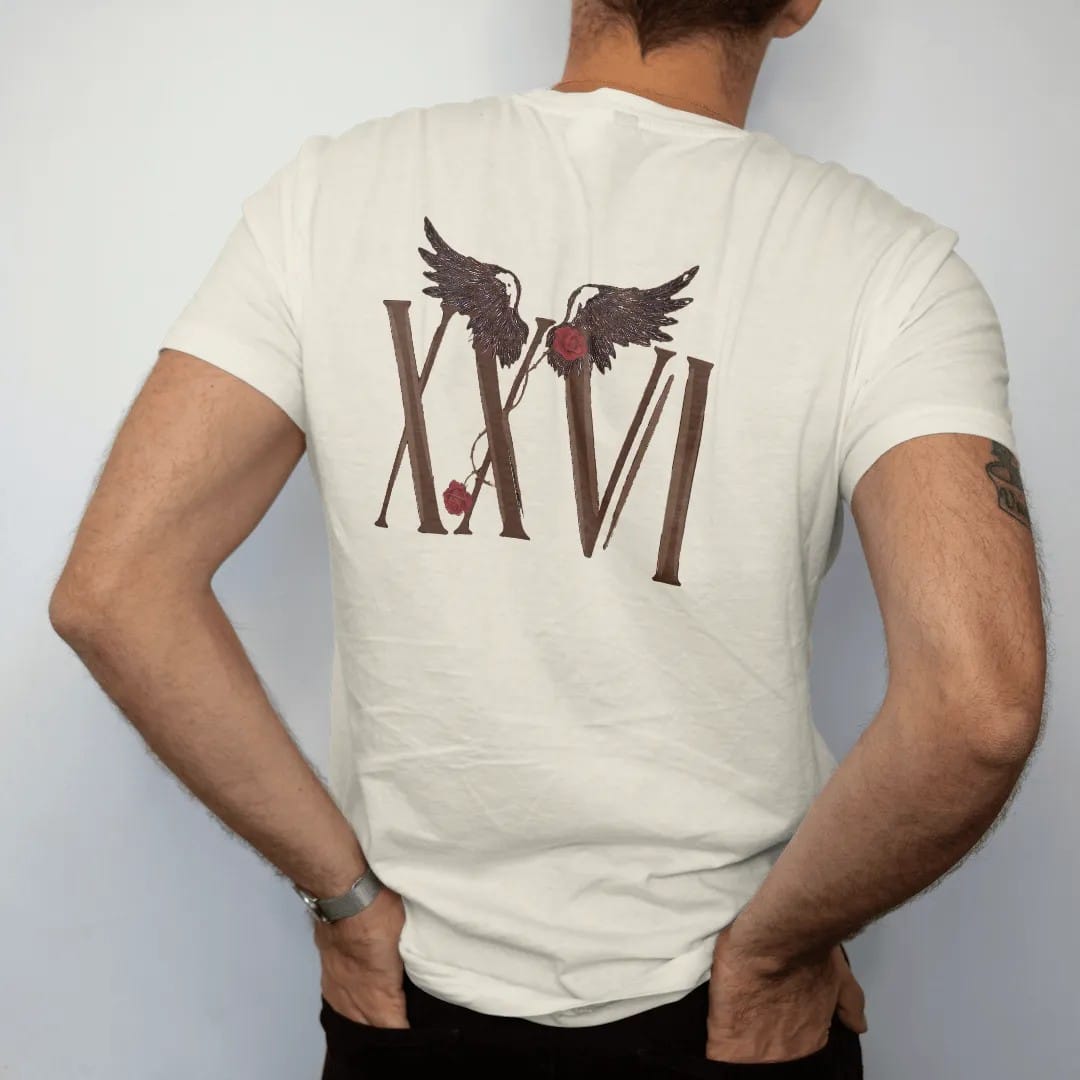 Man wearing a Ivory tee, seen from the back: Tall Roman serif numerals XXVI with a pair of feathered wings above and a thorny rose vine, in espresso and oxblood.