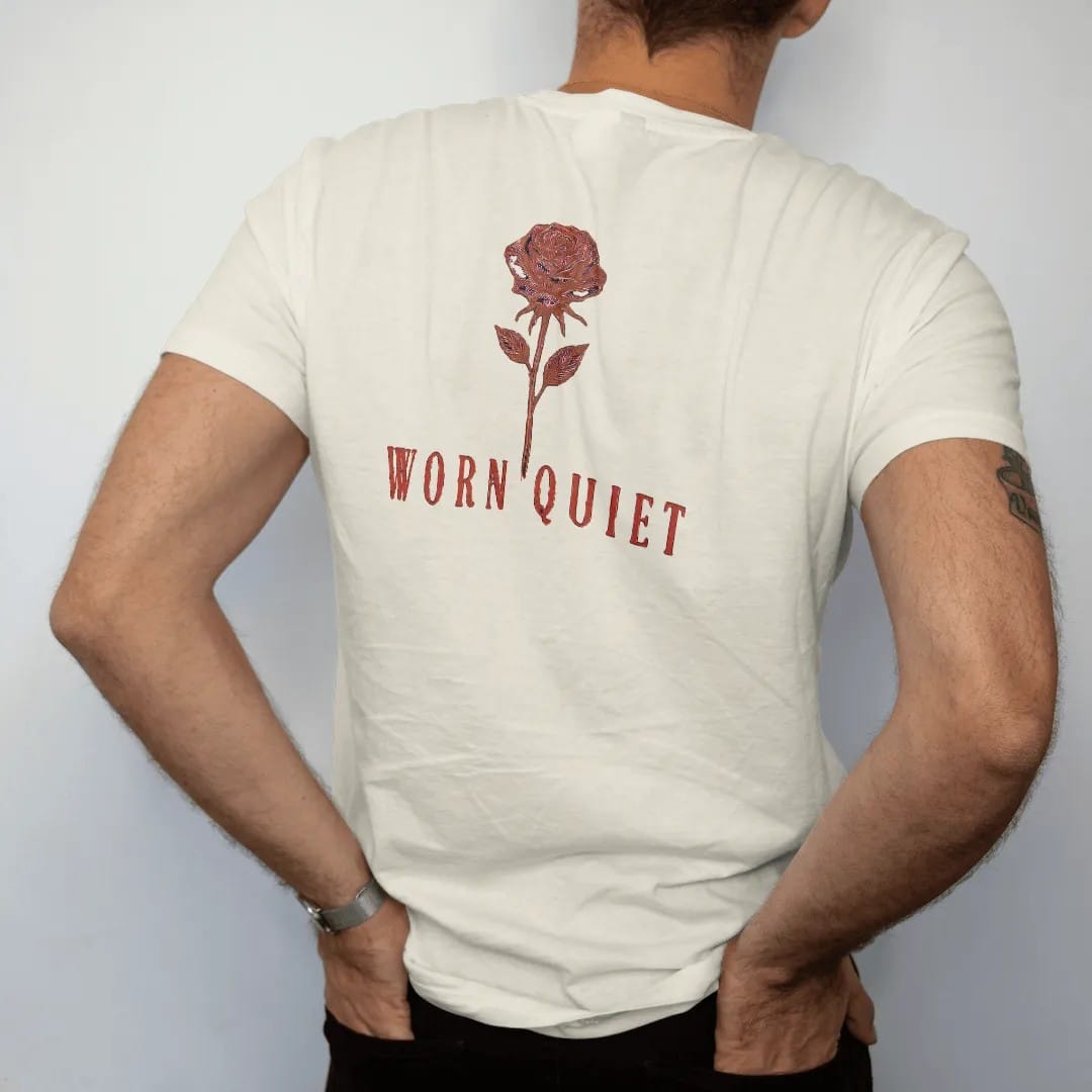 Man wearing a Ivory tee, seen from the back: a single fine-line long-stemmed rose above Worn Quiet in large widely spaced didone serif capitals, in espresso and oxblood.