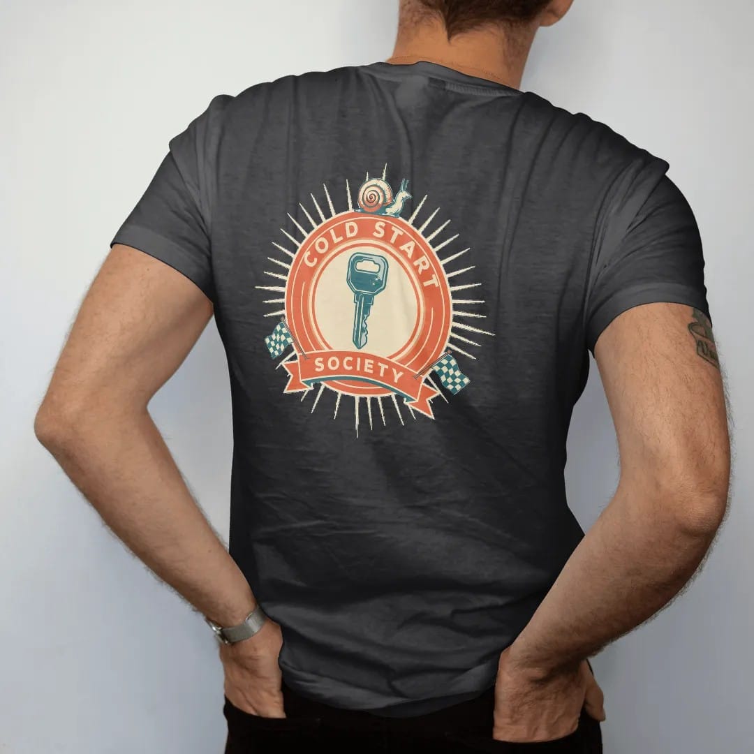 Man wearing a Black tee, seen from the back: a racing roundel with a frosted ignition key and a small turbo snail, Cold Start arched on top and Society on a bottom banner, in cream, orange, yellow and teal.