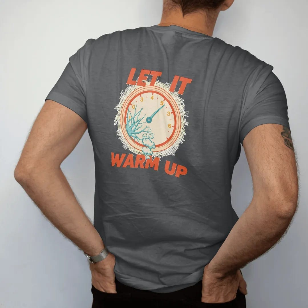 Man wearing a Graphite tee, seen from the back: a frosted vintage tachometer at high idle with small exhaust puffs and stacked Let It Warm Up lettering, in cream, orange, yellow and icy teal.