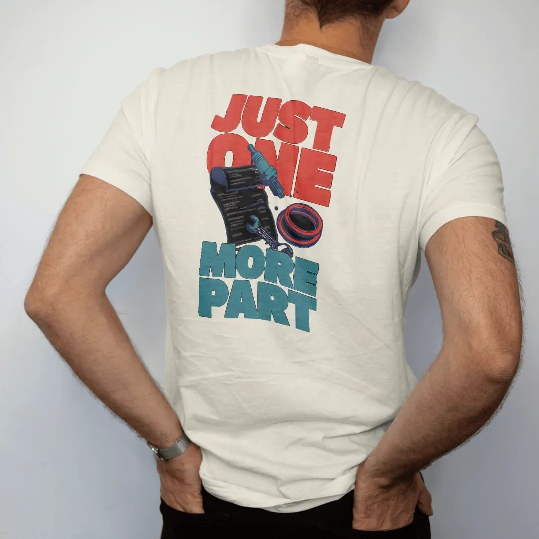 Man wearing a Ivory tee, seen from the back: a long curling parts-store receipt spilling a spark plug, gasket and wrench, with Just One More Part in stacked letters, in charcoal, rally red, teal and navy.
