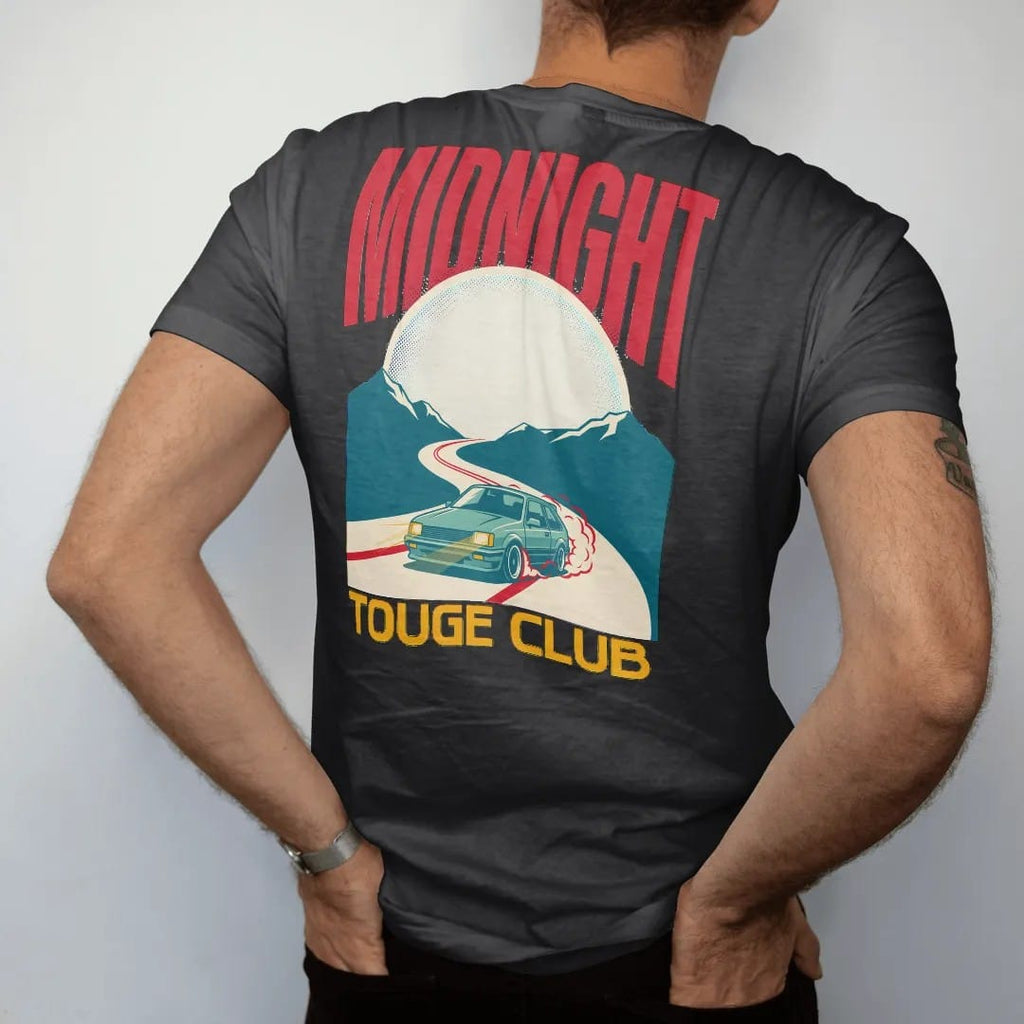 Man wearing a Black tee, seen from the back: a generic 90s hatchback drifting a moonlit mountain hairpin in a Japanese poster layout with Midnight Touge Club lettering, in cream, red, yellow and teal.
