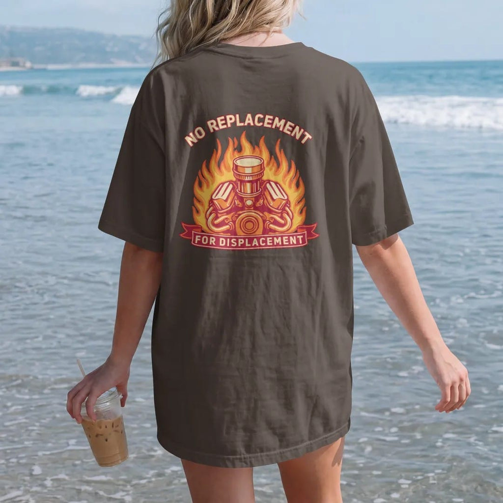 Woman on the beach in a Espresso tee, back view: a chrome-topped generic V8 engine with flames behind it, No Replacement arched above and For Displacement on a banner, in cream, orange, yellow and red.
