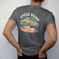 Man wearing a Graphite tee, seen from the back: a slammed generic sedan crawling over a big speed bump with sparks under the front lip, Speed Bump Survivor lettering, in yellow, cream, orange and teal.