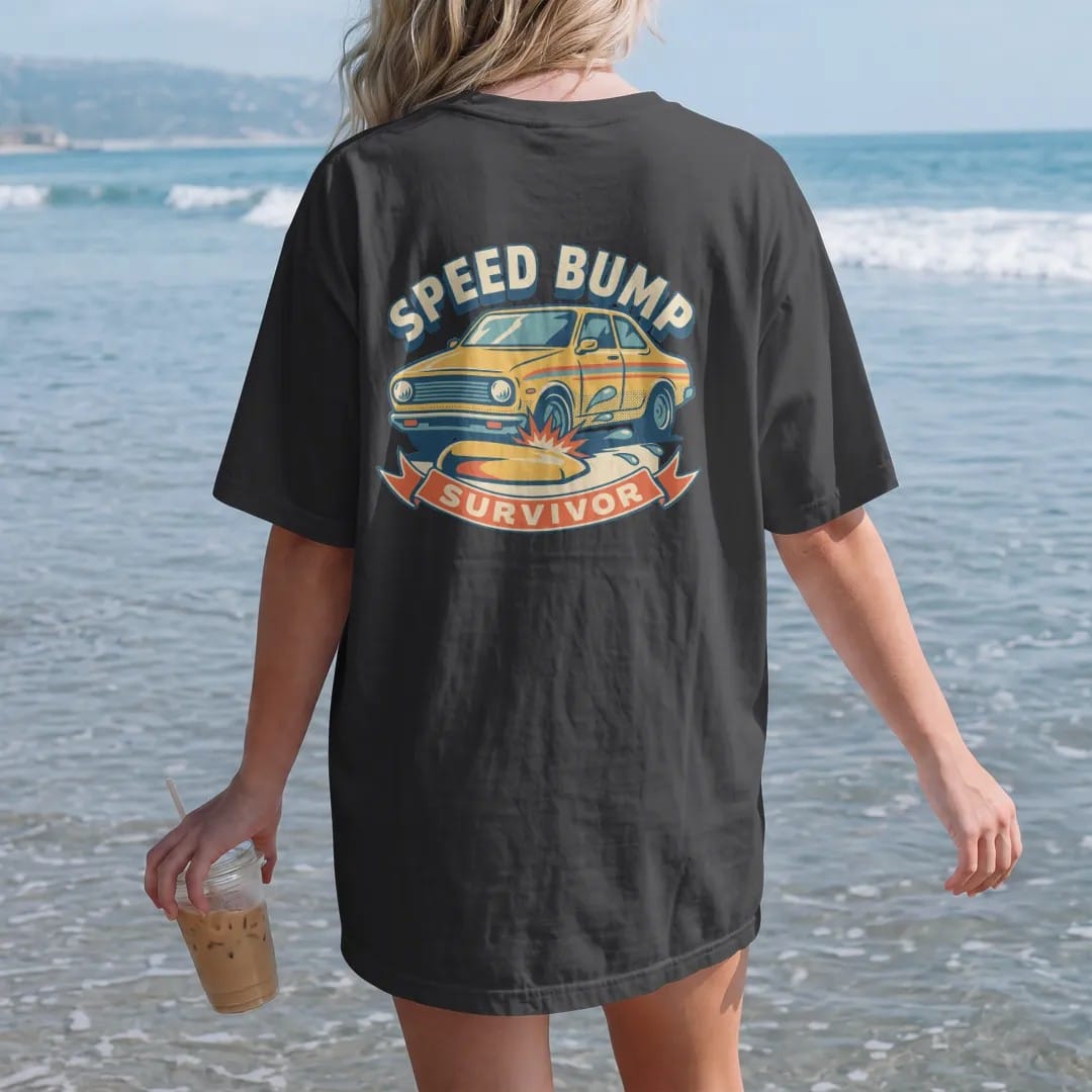 Woman on the beach in a Black tee, back view: a slammed generic sedan crawling over a big speed bump with sparks under the front lip, Speed Bump Survivor lettering, in yellow, cream, orange and teal.
