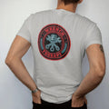 Man wearing a Granite tee, seen from the back: a round vintage badge with crossed wrenches over a piston and laurel leaves, Wrench arched over Therapy, in charcoal, rally red and teal.