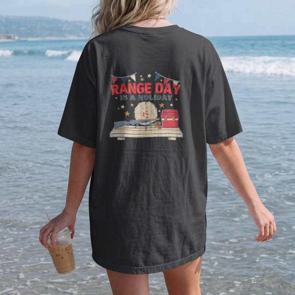 Woman on the beach in a Black tee, back view: a generic rifle and pistol resting on a shooting bench by a cooler with a target and bunting behind, Range Day Is A Holiday lettering, in brass gold, cream, red and blue.