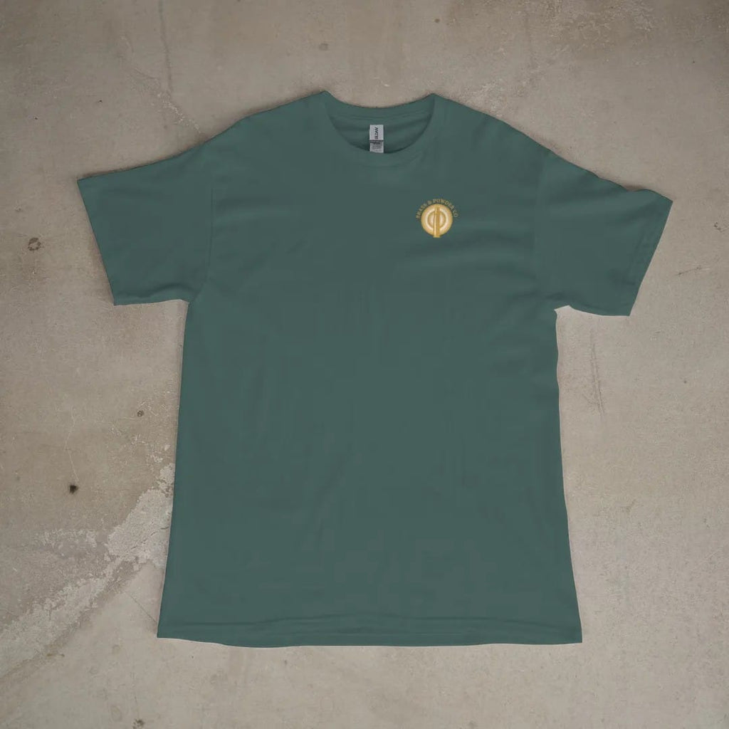 Front of a Blue Spruce tee laid flat, with the small Brass & Powder Co. logo on the left chest.