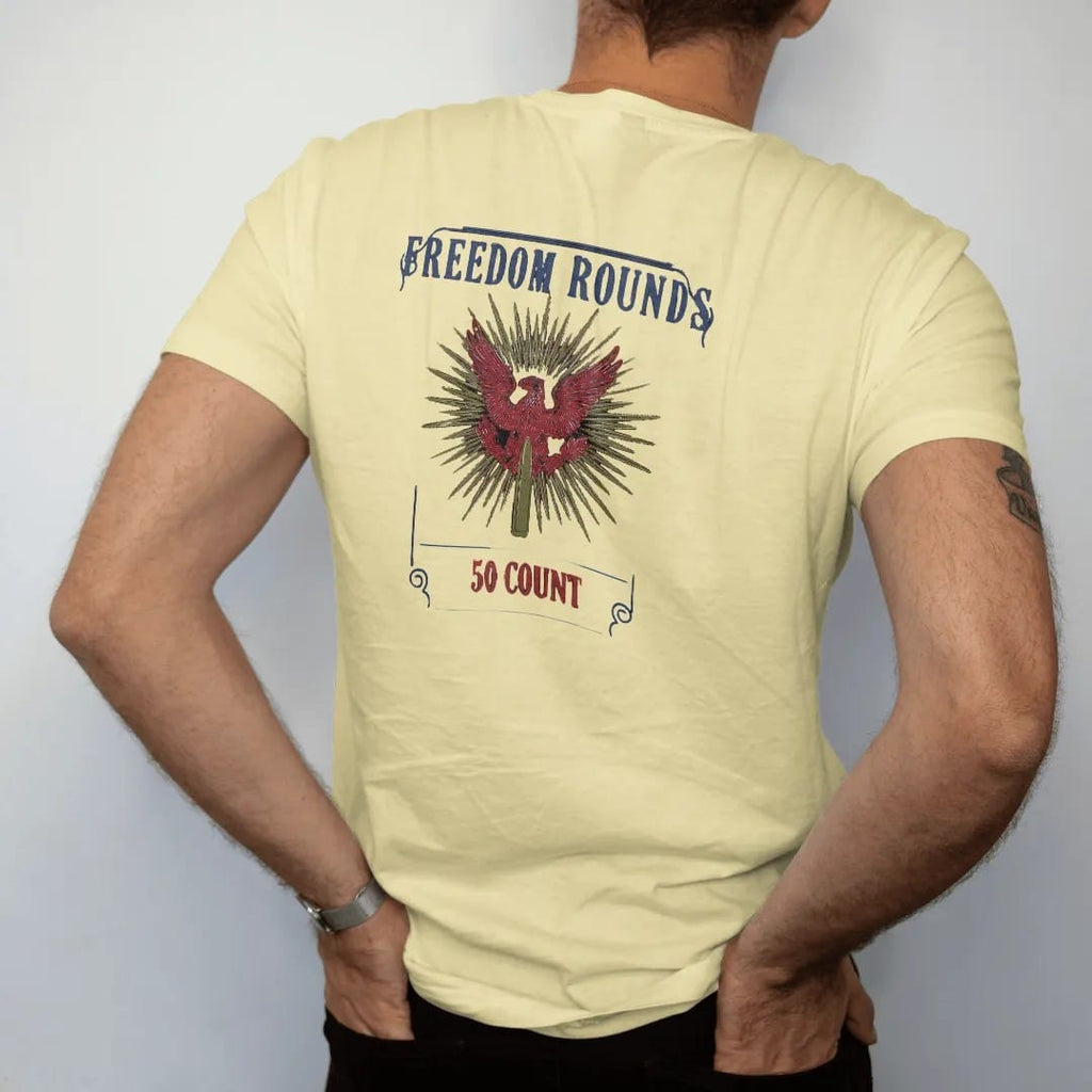 Man wearing a Butter tee, seen from the back: a vintage ammo-box label with ornate corners, a red eagle and one brass cartridge on starburst rays, Freedom Rounds above and 50 Count below.