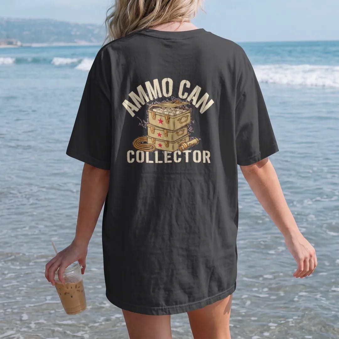 Woman on the beach in a Black tee, back view: a stack of three military-style ammo cans with one open, beside a rope coil and flashlight, Ammo Can Collector in stencil, in sand khaki, brass gold, cream and red.