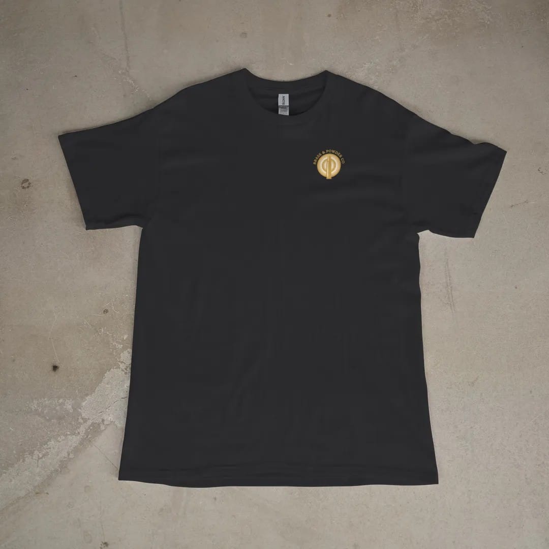 Front of a Black tee laid flat, with the small Brass & Powder Co. logo on the left chest.