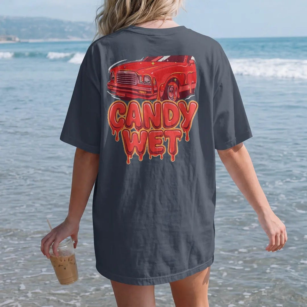 Woman on the beach in a Midnight tee, back view: glossy candy red paint dripping off a car hood with Candy Wet in big dripping letters, in red, silver, orange and lime.