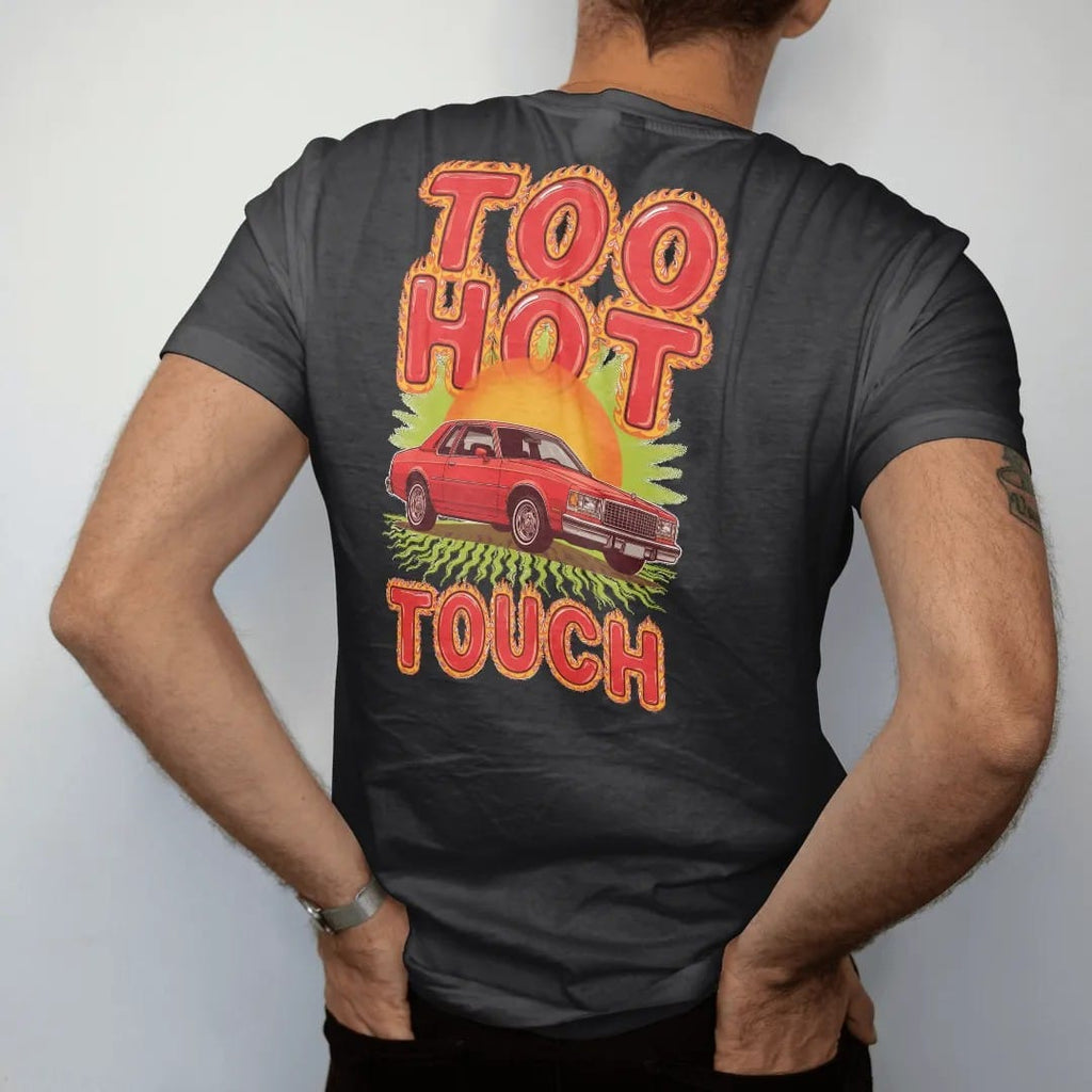 Man wearing a Black tee, seen from the back: a boxy 80s sedan on big chrome rims on shimmering hot asphalt under a blazing sun, with Too Hot over To Touch in flame-edged letters.