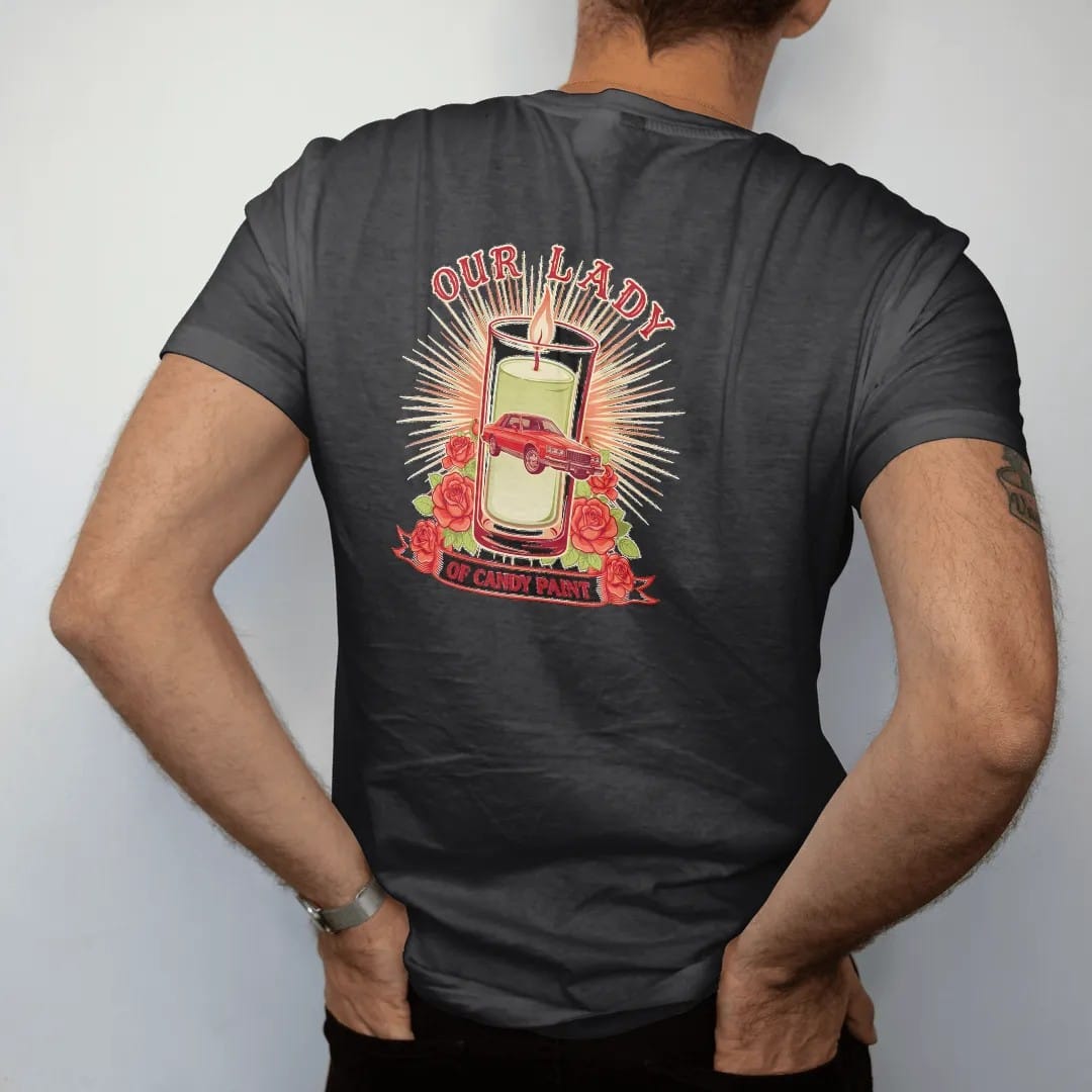 Man wearing a Black tee, seen from the back: a prayer-candle parody: a glowing votive with a boxy candy-red sedan on chrome wheels, roses and rays, Our Lady above and Of Candy Paint on a ribbon.