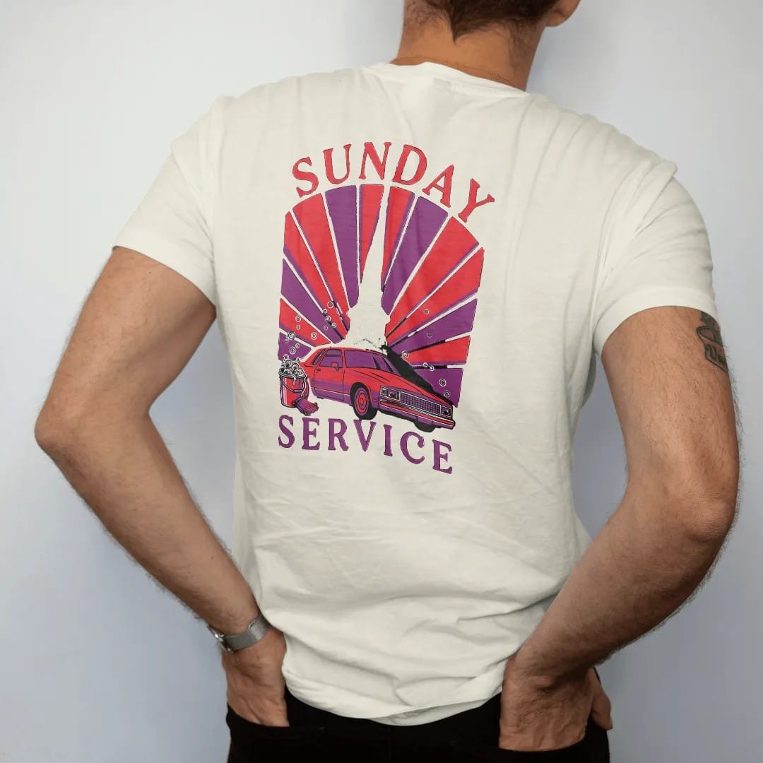 Man wearing a Ivory tee, seen from the back: a church steeple behind a boxy sedan on chrome rims being washed with a soap bucket and mitt, under Sunday and over Service, in deep red, purple and gunmetal.