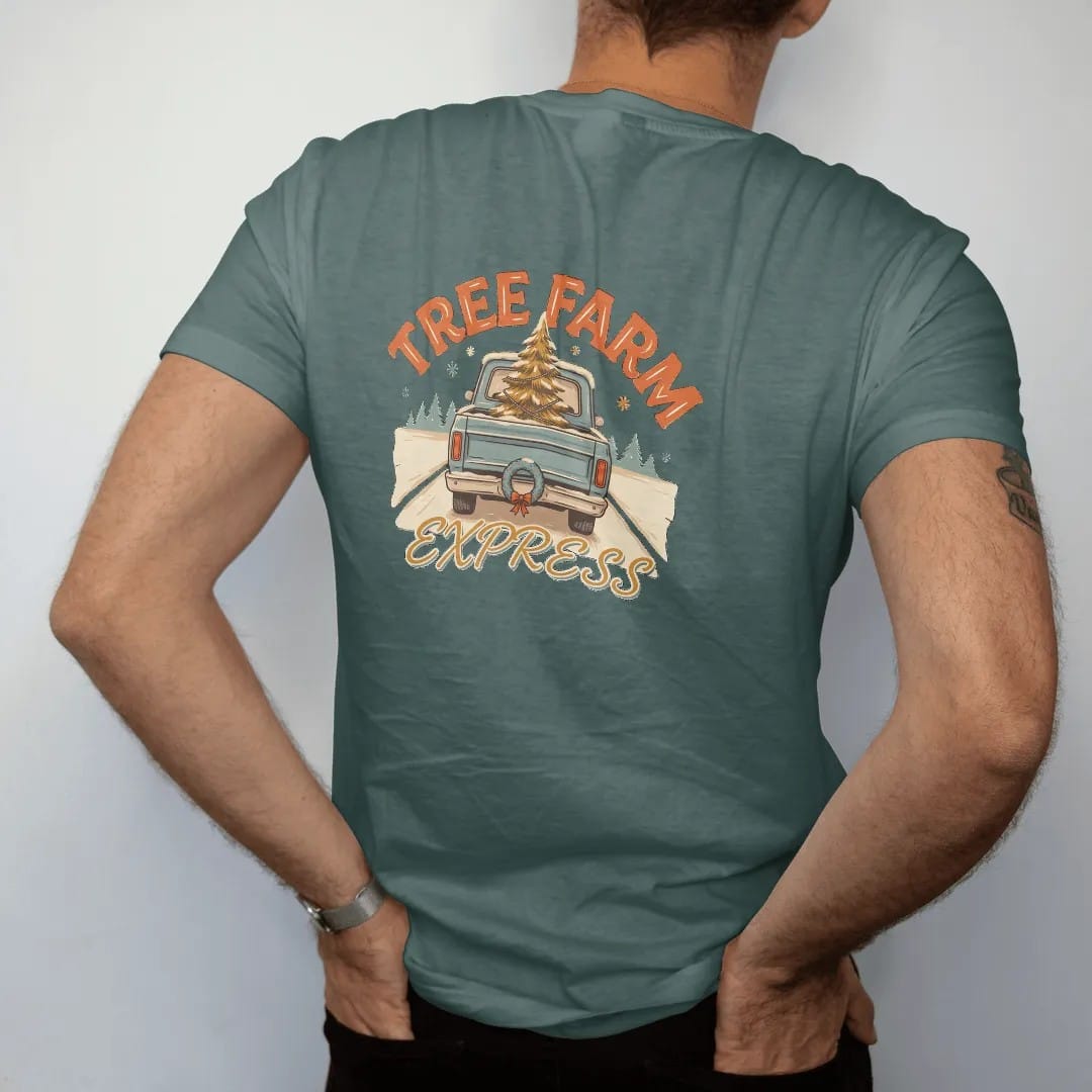 Man wearing a Blue Spruce tee, seen from the back: a square-body pickup on a snowy road with a Christmas tree in the bed and a wreath, under Tree Farm and over Express in retro script.