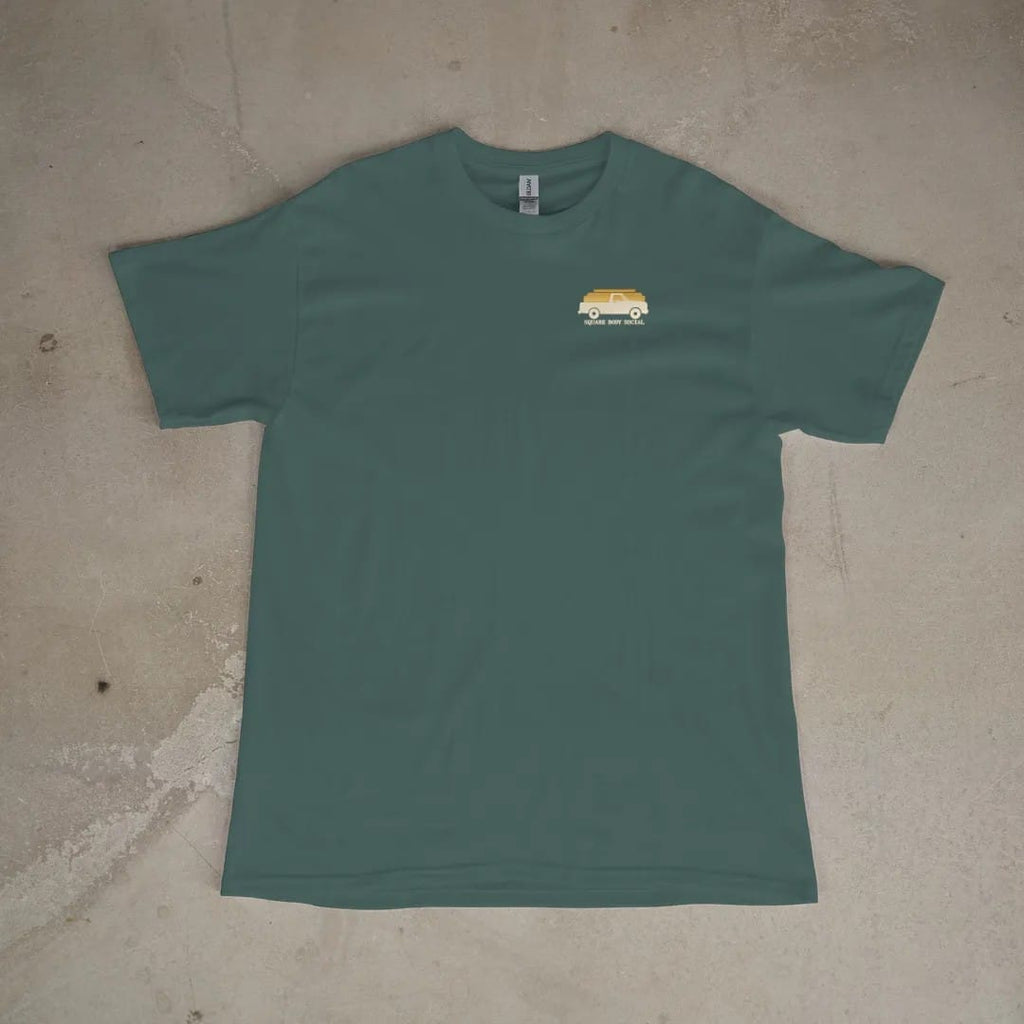 Front of a Blue Spruce tee laid flat, with the small Square Body Social logo on the left chest.