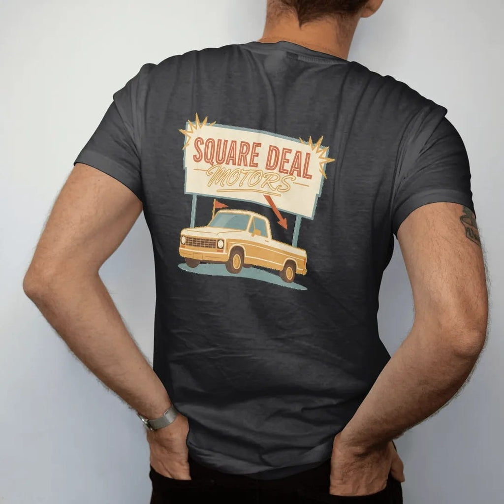 Man wearing a Black tee, seen from the back: a retro roadside dealership sign with starbursts over a square-body pickup with a sale flag, reading Square Deal over Motors.