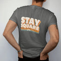 Man wearing a Pepper tee, seen from the back: a tiny square-body pickup riding 70s sunset stripes under Stay Square in giant cream block letters with an orange and gold drop shadow.