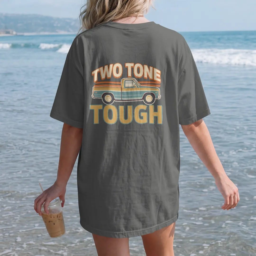 Woman on the beach in a Pepper tee, back view: a two-tone square-body pickup split by chrome trim in front of 70s stripes, under Two Tone and over Tough.