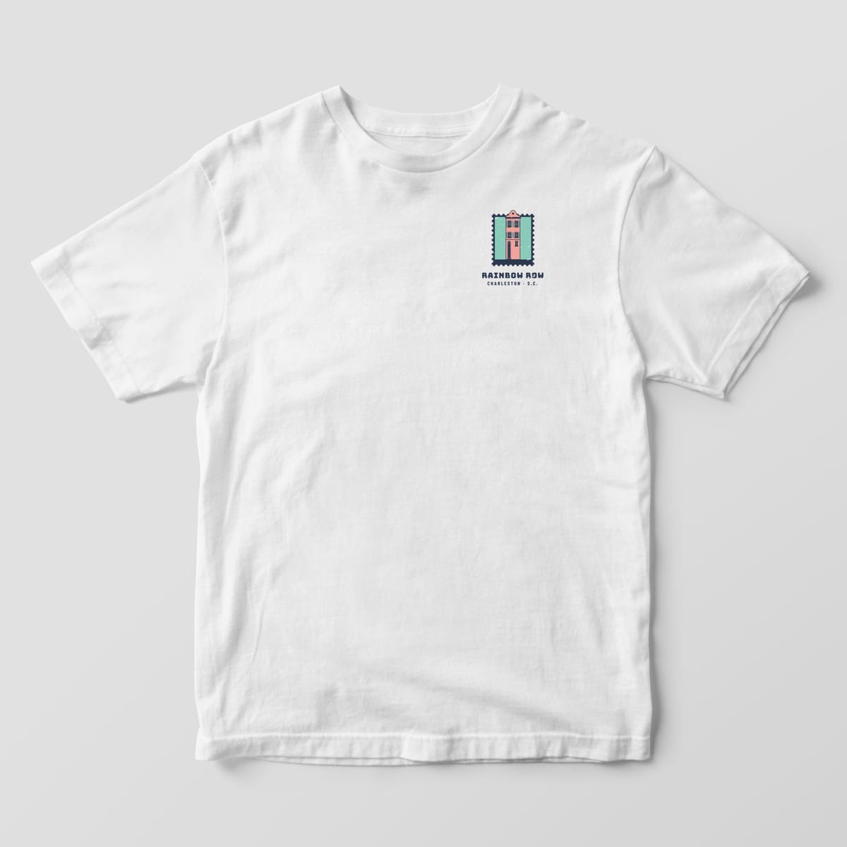Front of a White Comfort Colors 1717 tee with a small left-chest postage stamp of a pink row house and the words Rainbow Row, Charleston S.C.