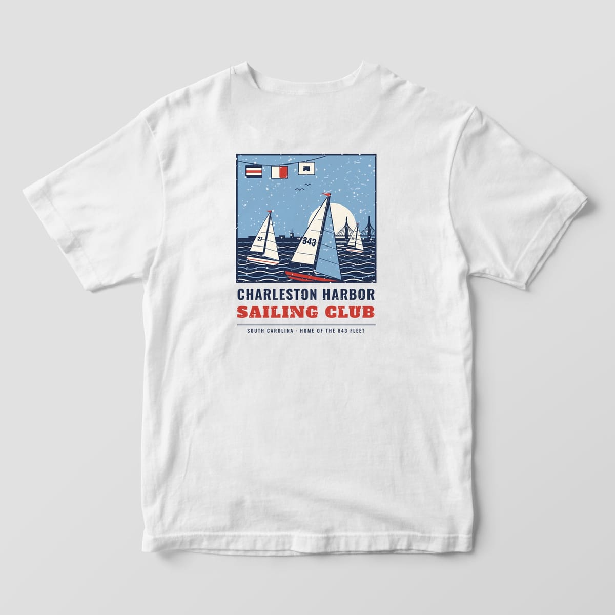 Back of a White Comfort Colors 1717 tee with a navy, red and sky blue poster of three sailboats racing at sunset above the words Charleston Harbor Sailing Club.