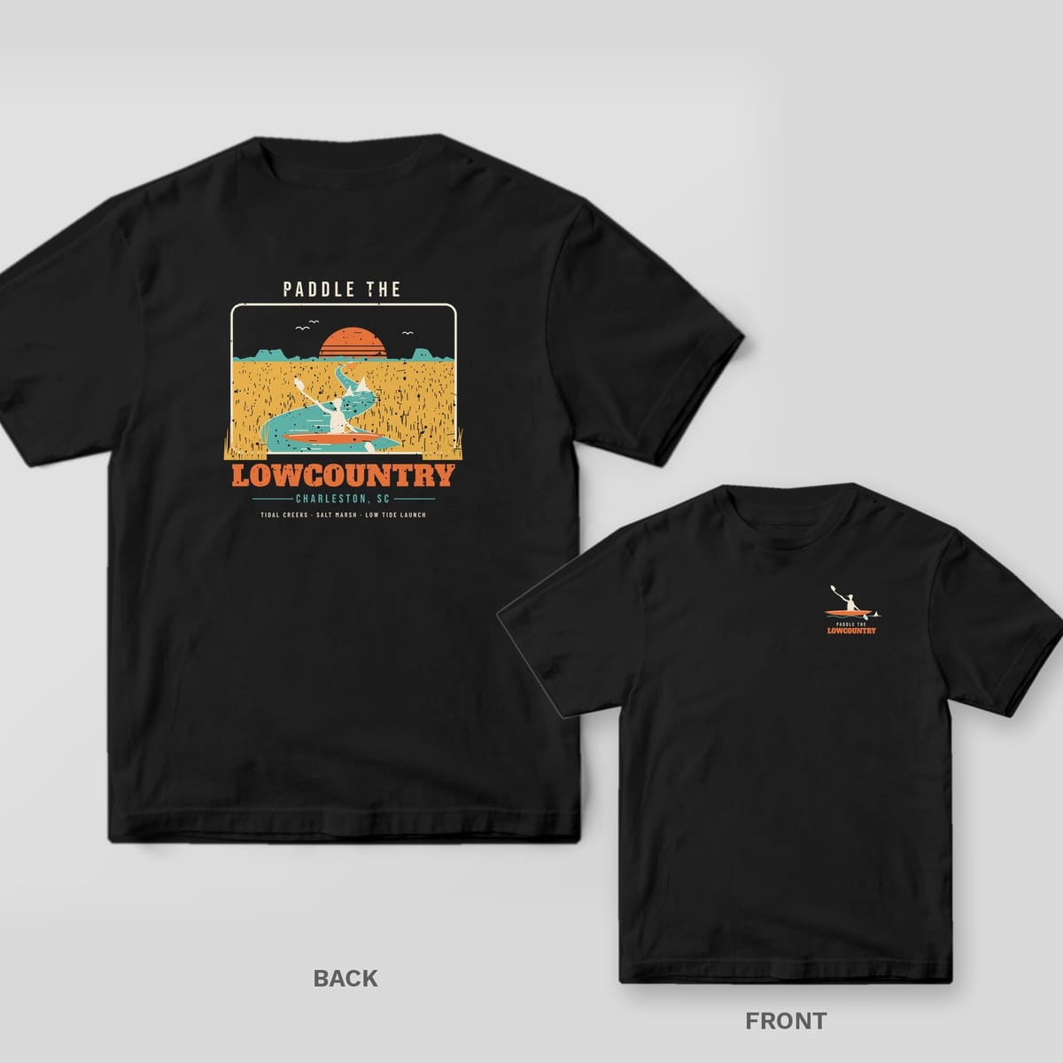 Black Comfort Colors tee shown back and front: a kayaker in a marsh creek at sunset on the back and a small kayak mark on the chest.