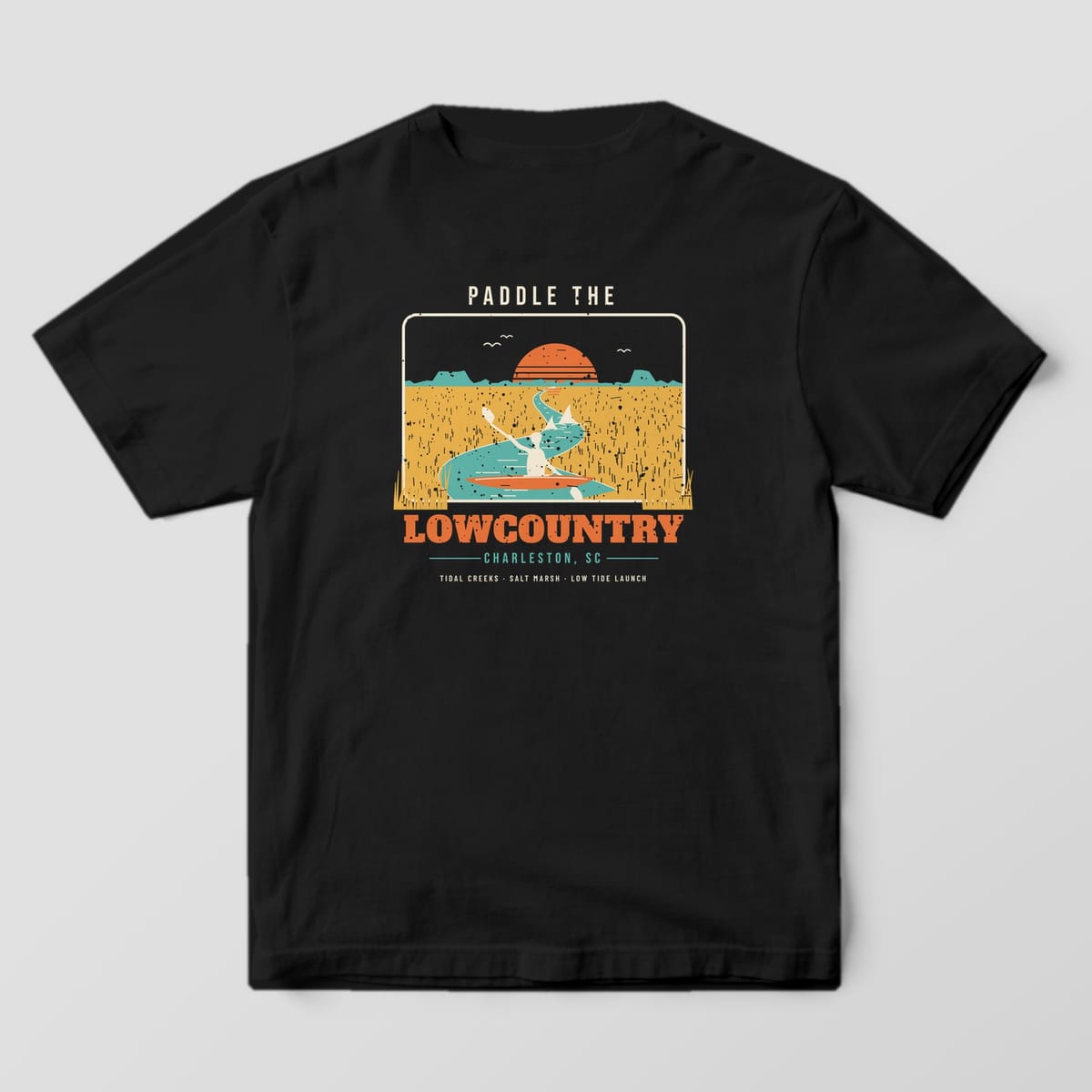 Back of a Black Comfort Colors 1717 tee with an orange, gold and teal scene of a kayaker and two dolphins in a tidal creek above the word Lowcountry.