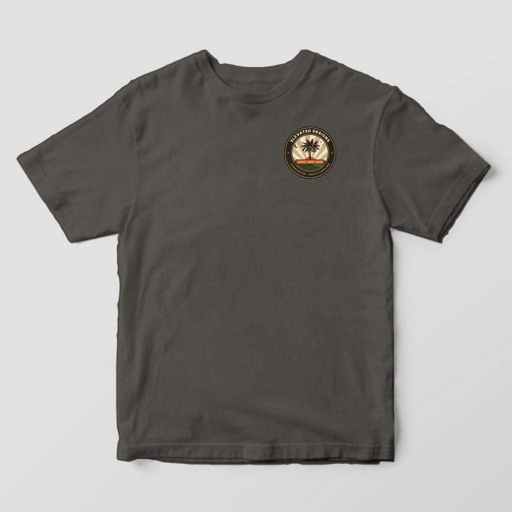 Front of a Pepper Comfort Colors 1717 tee with a small round left-chest crest reading ELEVATED DESIGNS and CHARLESTON · SOUTH CAROLINA around a palmetto tree and sunburst.