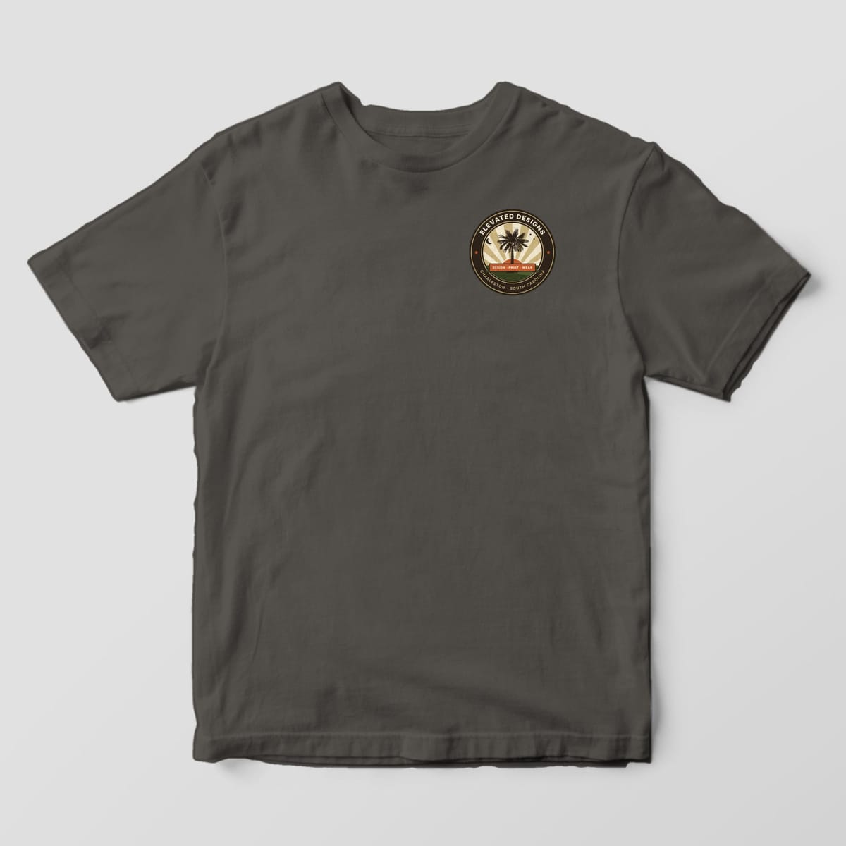 Front of a Pepper Comfort Colors 1717 tee with a small round left-chest crest reading ELEVATED DESIGNS and CHARLESTON · SOUTH CAROLINA around a palmetto tree and sunburst.