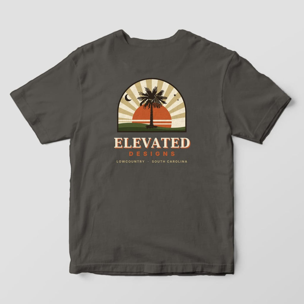 Back of a Pepper Comfort Colors 1717 tee with an arched-window scene of a palmetto in front of an orange sun and tan sunburst rays, a crescent moon and stars, with ELEVATED DESIGNS and LOWCOUNTRY · SOUTH CAROLINA below.