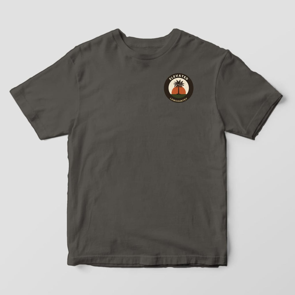 Front of a Pepper Comfort Colors 1717 tee with a small round left-chest badge reading ELEVATED and LOWCOUNTRY around a palmetto in front of an orange sun.