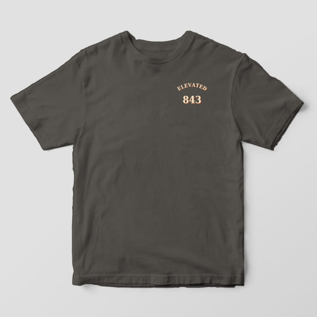 Front of a Pepper Comfort Colors 1717 tee with a small left-chest print of ELEVATED arched over 843 in cream with a rust shadow.