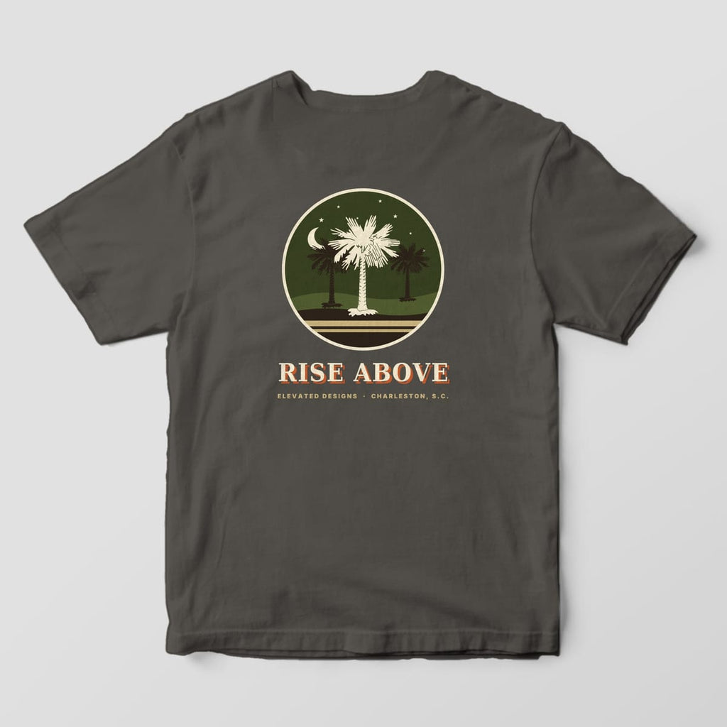 Back of a Pepper Comfort Colors 1717 tee with a round olive night scene of three palmetto trees under a crescent moon and stars, with RISE ABOVE and ELEVATED DESIGNS · CHARLESTON, S.C. below.