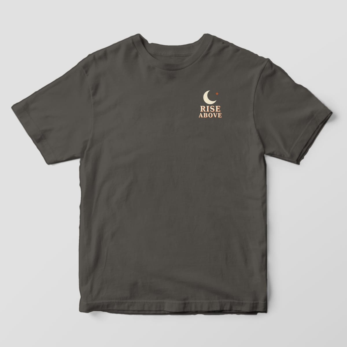 Front of a Pepper Comfort Colors 1717 tee with a small left-chest cream crescent moon and rust star above the words RISE ABOVE.