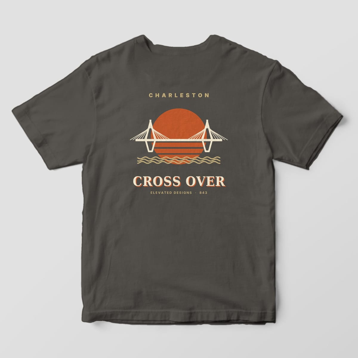 Back of a Pepper Comfort Colors 1717 tee with CHARLESTON above a cream cable-stayed bridge crossing a striped orange sun and tan wavy water, with CROSS OVER and ELEVATED DESIGNS · 843 below.