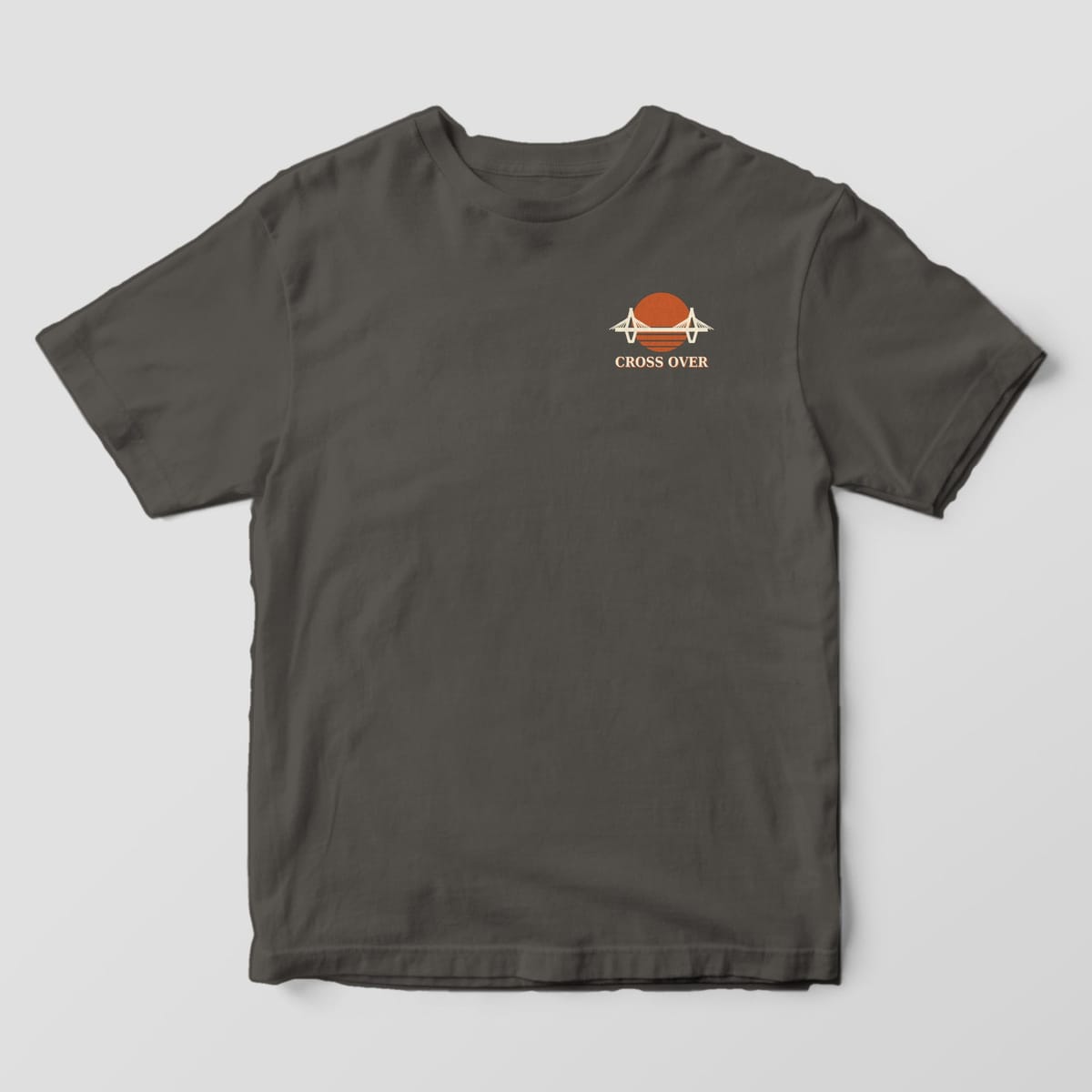Front of a Pepper Comfort Colors 1717 tee with a small left-chest cable-stayed bridge across a striped orange sun above the words CROSS OVER.