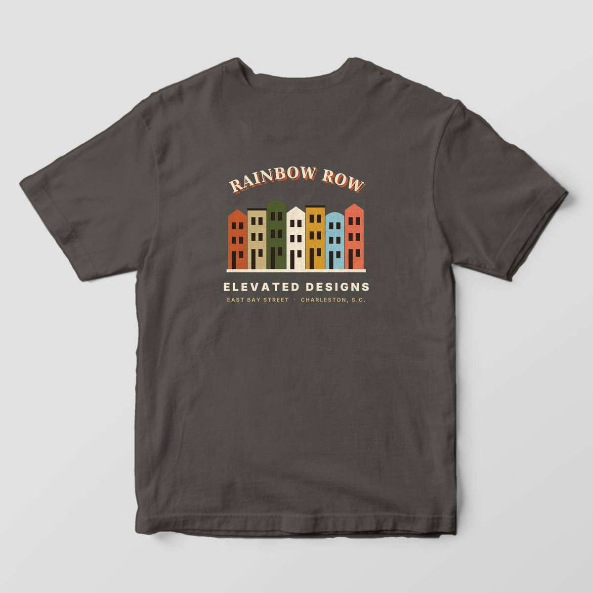 Back of a Pepper Comfort Colors 1717 tee with RAINBOW ROW arched over seven row houses in rust, tan, olive, cream, gold, light blue and coral, with ELEVATED DESIGNS and EAST BAY STREET · CHARLESTON, S.C. below.