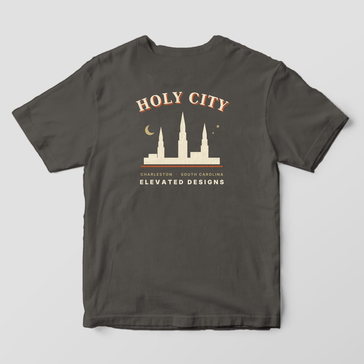 Back of a Pepper Comfort Colors 1717 tee with HOLY CITY arched over a cream skyline of three church steeples with a gold crescent moon and two stars, then CHARLESTON · SOUTH CAROLINA and ELEVATED DESIGNS.