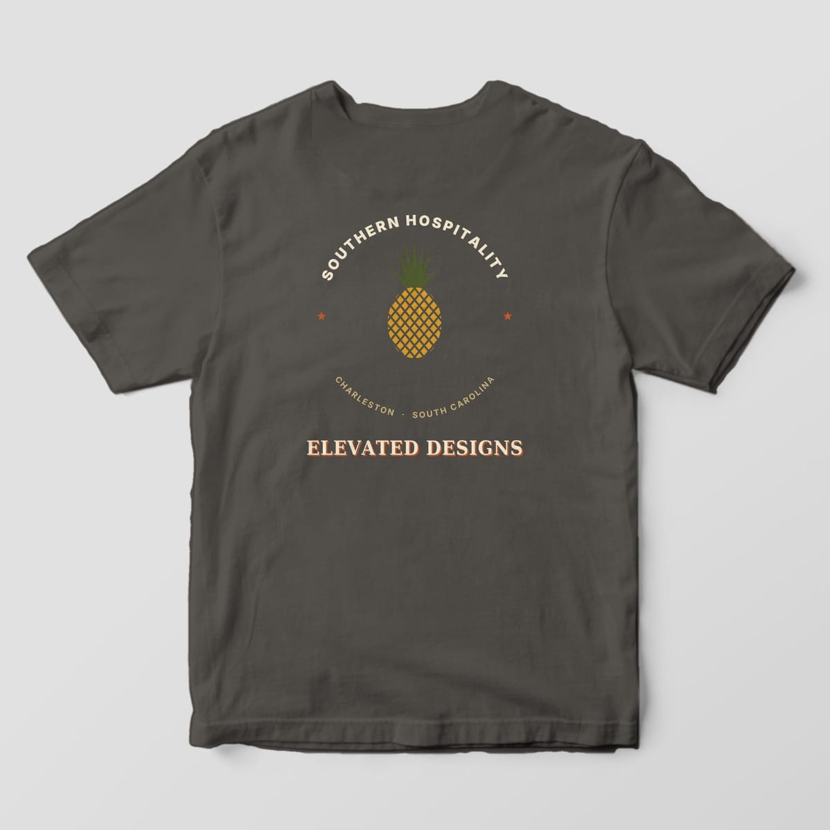 Back of a Pepper Comfort Colors 1717 tee with SOUTHERN HOSPITALITY arched over a gold pineapple with an olive crown, two rust stars, CHARLESTON · SOUTH CAROLINA and ELEVATED DESIGNS.