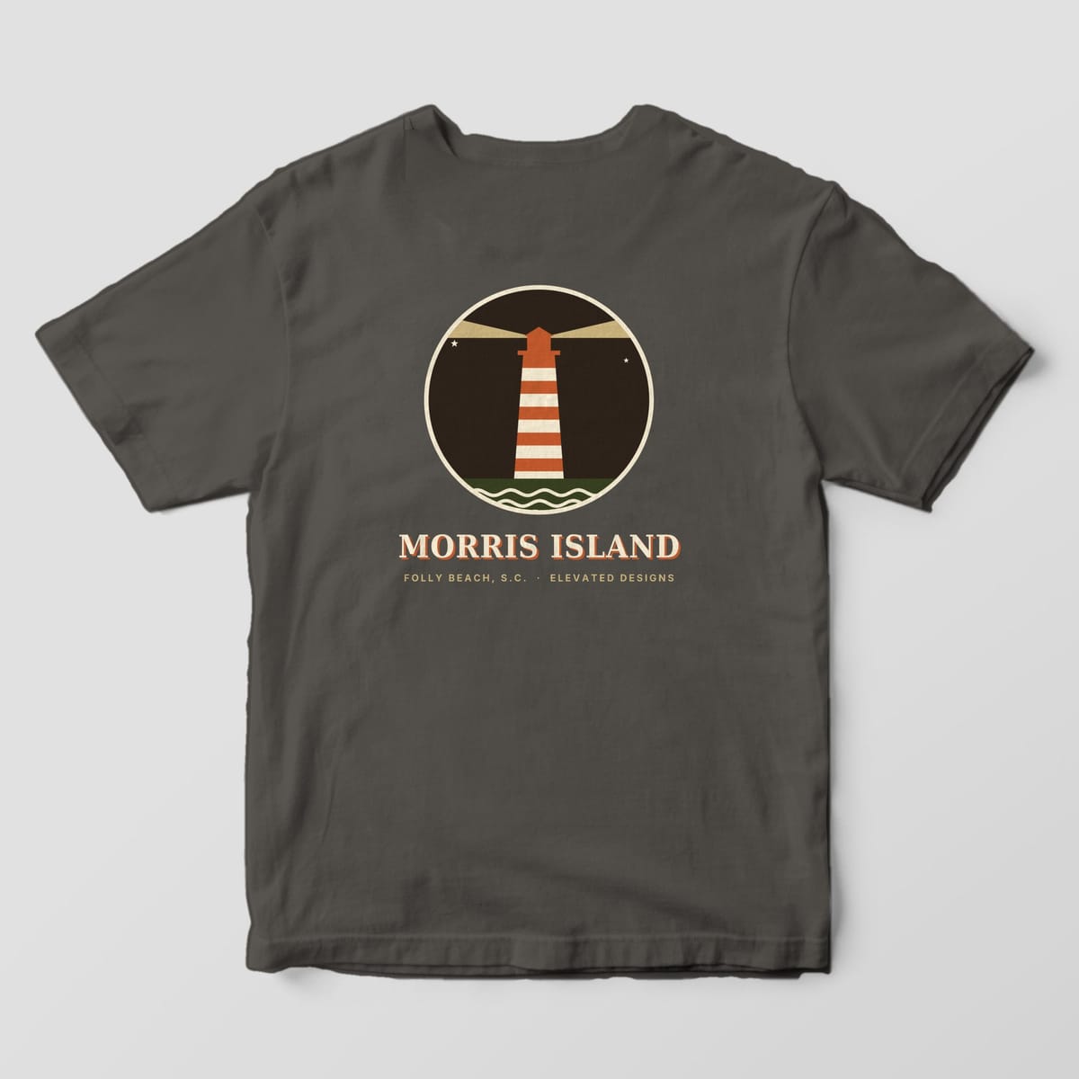 Back of a Pepper Comfort Colors 1717 tee with a round dark night badge of a rust-and-cream striped lighthouse with tan light beams and waves, above MORRIS ISLAND and FOLLY BEACH, S.C. · ELEVATED DESIGNS.